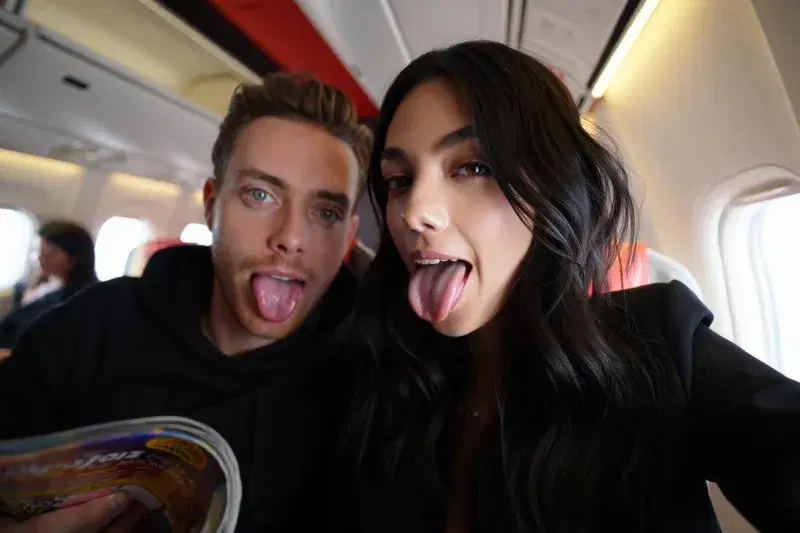 Real Reve Criar generation: an1ta, close-up selfie of two young adults inside an airplane cabin, both playfully sticki