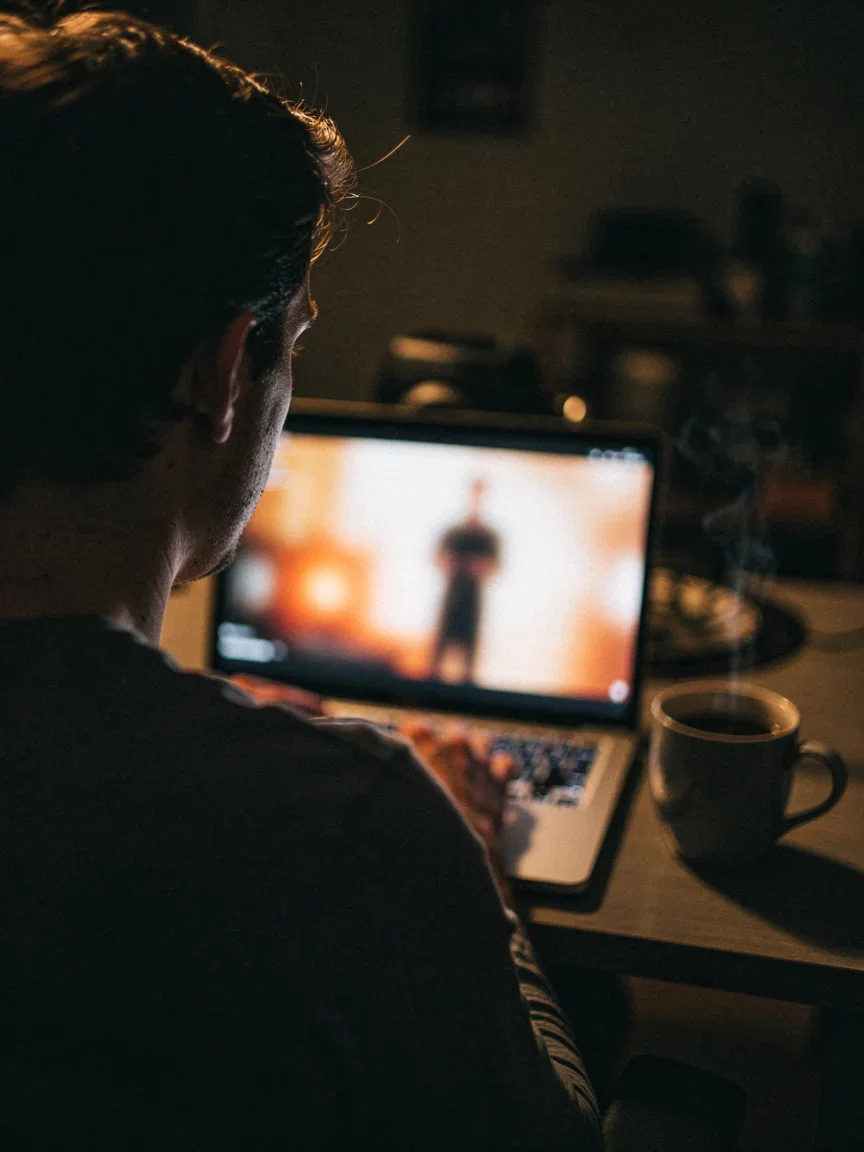 Over-the-shoulder view of a person watching a video sales letter on a laptop at night, the screen a soft blurred glow, generated on FluxoKit