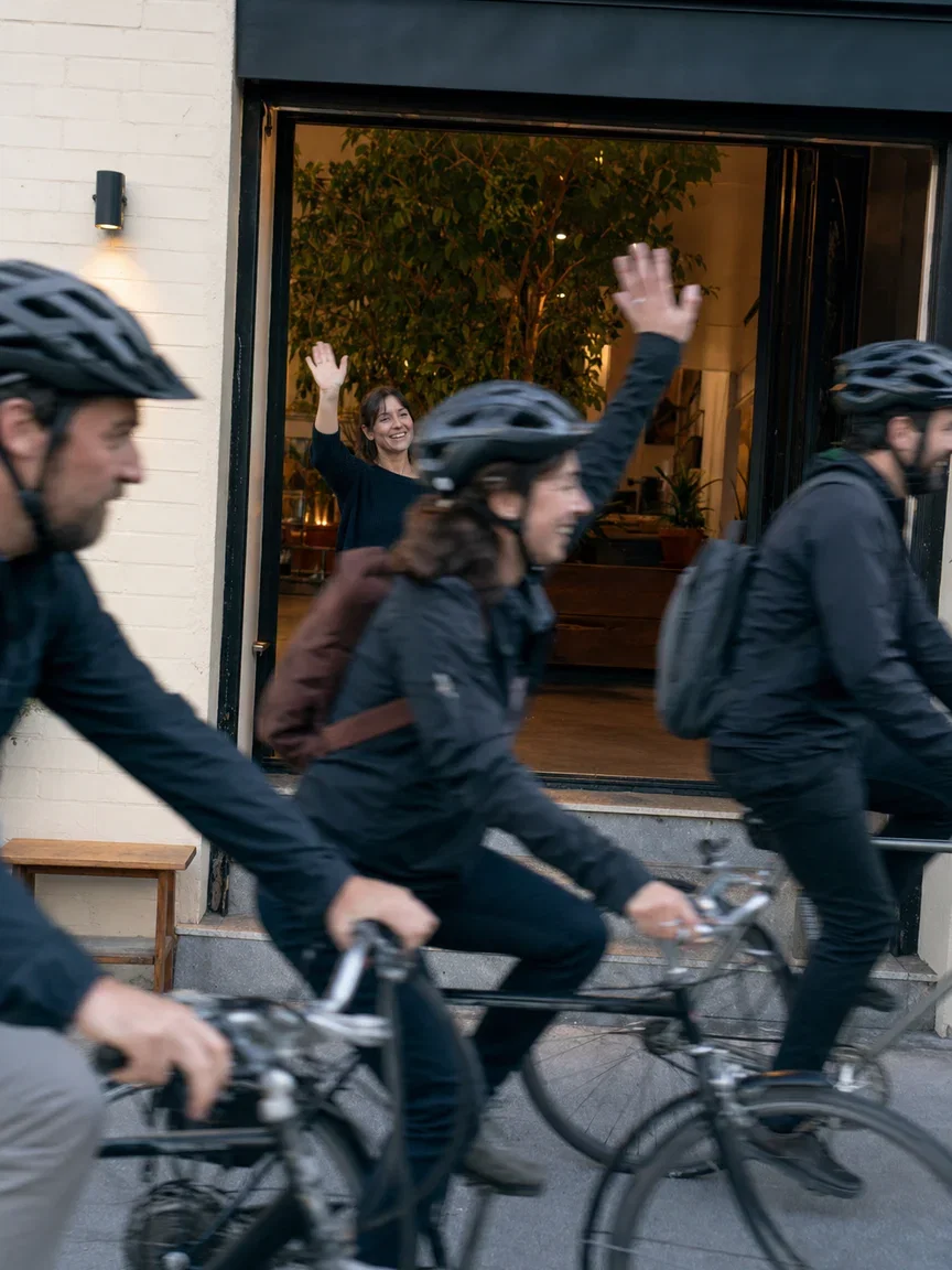 Morning bike commuters streaming past the shop with one rider waving, rendered with GPT Image 2 on FluxoKit