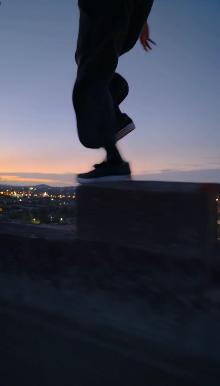 Leap silhouetted over the rooftop gap at dusk, beat frame from a Kling 2.6 clip on FluxoKit