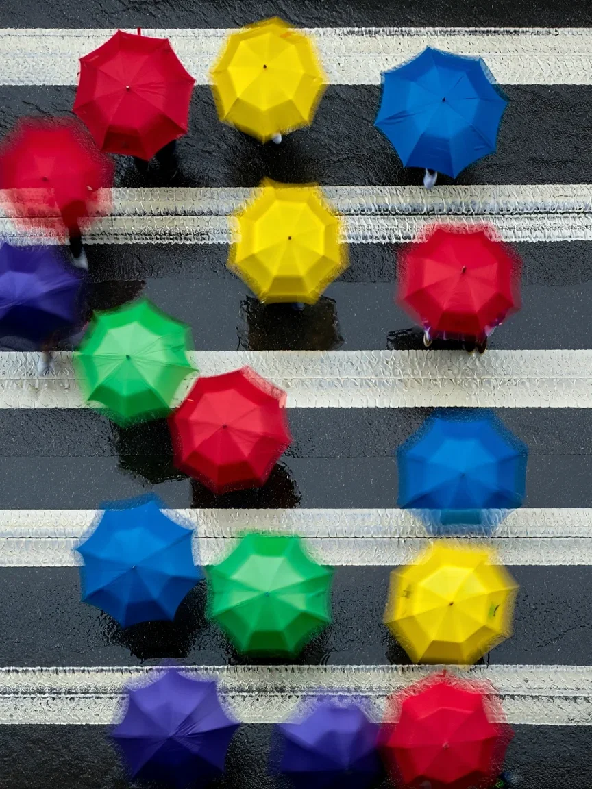 Overhead view of colorful umbrellas crossing a rain-slick crosswalk, generated with Reve on FluxoKit