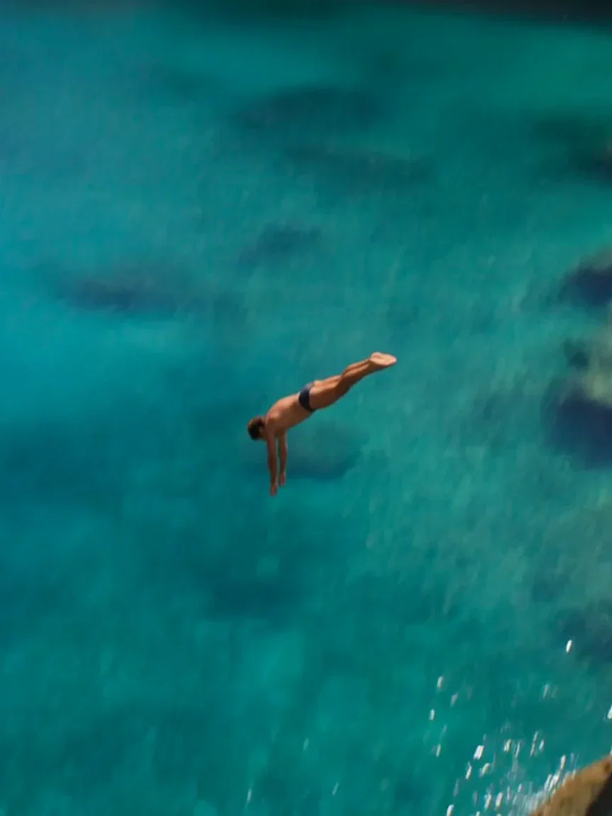 Cliff jumper mid-air over turquoise water, beat frame from a Seedance 2.0 clip on FluxoKit